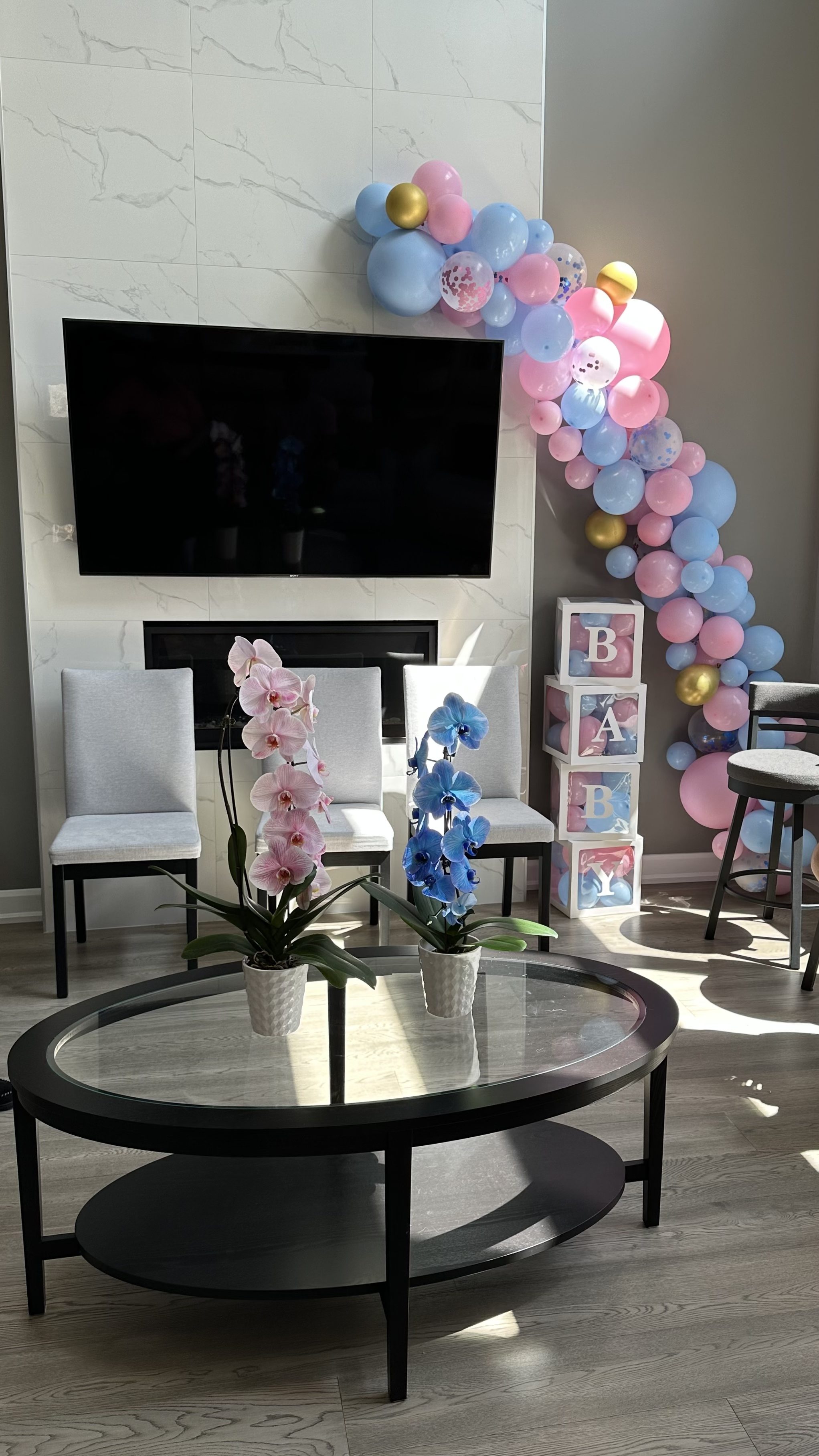 Decorations for the gender reveal party including blue and pink balloons, boxes that spell the word baby with balloons in them, and blue and pink plants.